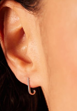 Boucle d'oreille en argent au design minimaliste, présentant une forme courbée. Une vue de près révèle une surface lisse et une finition brillante contre la peau.