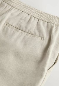 Pantalon en tissu beige avec un motif texturé subtil, doté d'une taille élastique et d'une poche arrière unique.