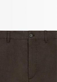 Pantalon en lin marron foncé avec fermeture à boutons et passants de ceinture, montrant la zone de la taille et la couture de l'ouverture avant.