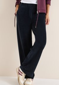 Pantaloni a gamba larga in corduroy blu navy con tessuto texturizzato, dotati di tasche frontali e cintura elastica; abbinati a sneakers beige e bordeaux.