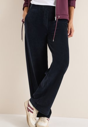 Pantalons en velours côtelé navy à jambes larges avec un tissu texturé, comprenant des poches avant et une taille élastique ; associés à des baskets beige et bordeaux.