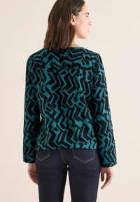 Langærmet bluse med et geometrisk mønster i turkis og sort, lavet af et glat stof med en afslappet pasform og rund halsudskæring.