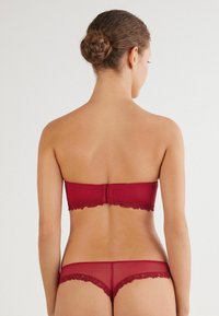 Rode bh zonder banden met kantafwerking en bijpassende doorschijnende rode string, met een gladde textuur en een aansluitend ontwerp, getoond vanuit de achterkant.