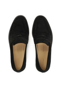 Mocasines de ante negro con un acabado suave, punta redondeada y detalles de costura sutiles. Plantilla de color marrón con logotipo y acentos de diseño mínimos.