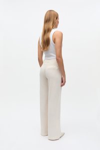 Kõrge vöökohaga beežist lina püksid laiade sääreosadega, millel on lihtne disain, peen tekstuur ja tagataskud.