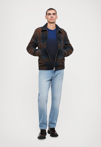 Wool blend jacket in dark blue and orange tones, featuring a zip closure, two pockets, and a collar, paired with light blue jeans and black shoes.
