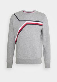 Grå langærmet sweatshirt med diagonale marineblå, hvide og røde striber på tværs af brystet og "Tommy Hilfiger" logoet øverst til højre.
