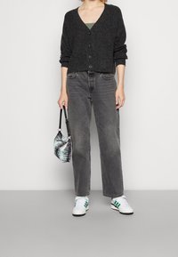 Ciemnoszary kardigan na guziki na zielonym topie, zestawiony z wysokim stanem szarych dżinsów i białymi sneakersami z zielonymi akcentami. Mała torebka w wzory.