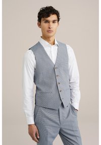 Chaleco de espiga gris en un corte entallado, con cinco botones, dos bolsillos frontales y un pico agudo, llevado sobre una camisa blanca.