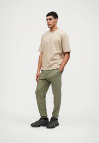 Beige short-sleeve t-shirt paired with olive green joggers, featuring a relaxed fit and side stripes. Black sneakers complete the look.