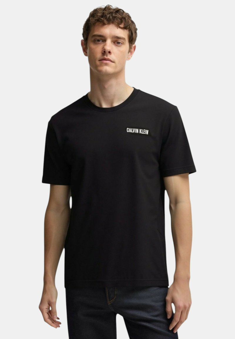 T-shirt nera in cotone, a maniche corte, con collo tondo, caratterizzata da un logo bianco "CALVIN KLEIN" sul lato sinistro del petto. Design elegante e informale.