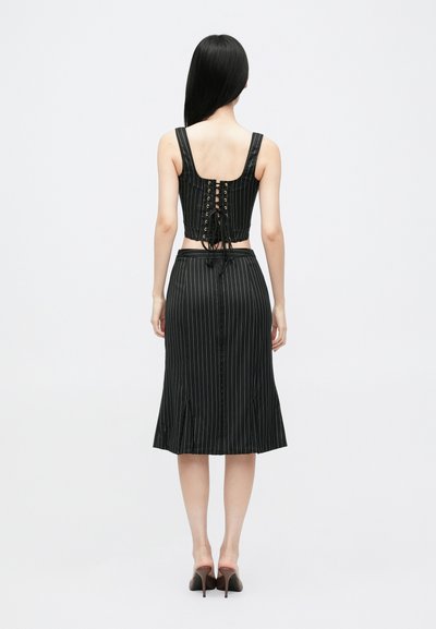 Juodas, dryžuotas trumpas viršus su nėriniais nugaros, derinamas su juoda, iki kelių siekiančia sijoną, turinčia plyšį ir mygtukų uždarymą.