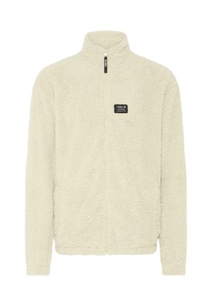 Krémszínű bolyhos dzseki, magas gallérral, teljes hosszúságú cipzárral és textúrált felülettel. A mellrészen egy kis márka logó található.