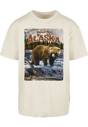 Krém színű pamut póló, amelyen egy barna medvét ábrázoló grafika látható vízben, hegyek és fák között, felirattal: "Alaszka" és "Az Utolsó Határ".