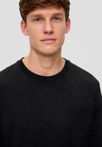 Schwarzes T-Shirt mit Rundhalsausschnitt aus weichem Stoff, ausgestattet mit einer kleinen Brusttasche und einer dezenten Textur. Klassische Passform mit entspanntem Design.