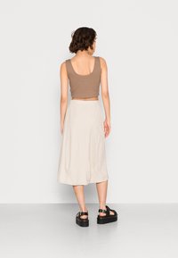 Top corto marrón con textura acanalada, falda midi beige de textura suave y sandalias negras de plataforma. Vista desde atrás sobre un fondo liso.