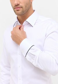 Witte overhemden gemaakt van een gladde stof, met een contrasterende zwarte afwerking op de kraag en manchetten, en klassieke knoopsluiting.