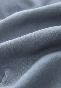 Tissu bleu clair et doux avec une texture de tricot visible et des plis légers créant des contours lisses et fluides.