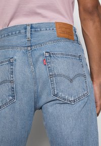 Ljusblå denimjeans med hög midja, två bakfickor och en brun läderlapp på midjebandet med märkesinformation. Röd logotab.