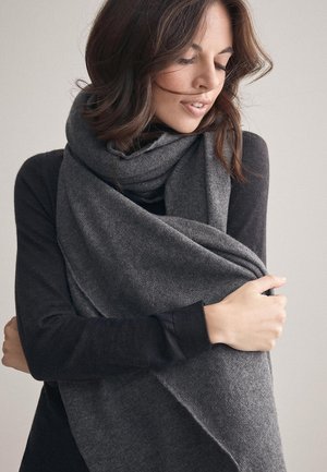 Mörkgrå, överdimensionerad scarf av mjukt tyg, svept runt halsen. Modellen bär en långärmad topp som visar scarfens textur och värme.