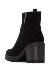 Botín de ante negro con un tacón bloque texturizado negro y cremallera lateral. Presenta una punta redondeada y una superficie suave y lisa.