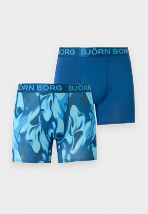 Άνδρας χωρίς πουκάμισο, όρθιος, ξυπόλυτος, φορώντας μπλε σκαλιστά μποξεράκια με λουράκι μέσης "BJÖRN BORG" σε απλό λευκό φόντο.