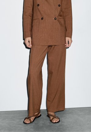 Brun linned dobbeltradet blazer med matchende brede bukser, der har struktureret stof, samt brune sandaler med tynde stropper.