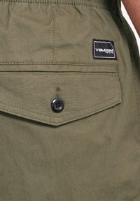 Shorts vert olive avec une poche arrière, dotés d'un bouton noir et d'une étiquette "VOLCOM". Le matériau a une finition douce et texturée.