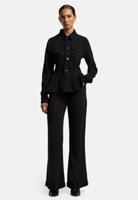 Giubbotto di jeans nero con colletto, chiusura a bottoni e due tasche sul petto. Abbinato a pantaloni neri a gamba larga e stivali neri.