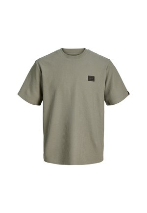 Lühikeste varrukatega oliivrohelise tekstuuriga ümara kaelusega T-särk, mille vasakul rinnal on väike must-kuldne ristkülikukujuline plaastr.