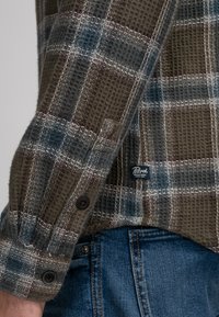 Groen en blauw geblokt shirt met een geweven structuur, voorzien van zwarte knopen en een logo-patch aan de onderkant. Perfect te combineren met jeans.