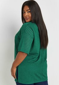 Grön kortärmad topp med texturerade ränder, med avslappnad passform, sidofickor och en något längre bakdel för komfort.