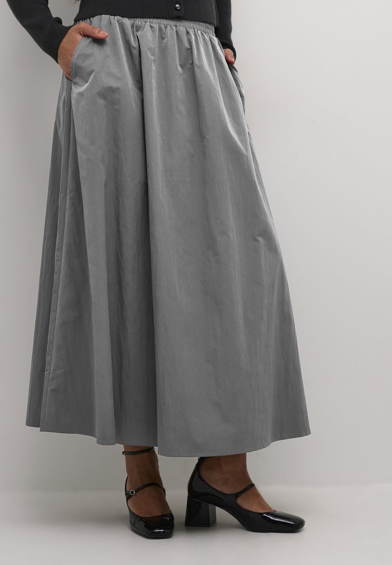 Grijze maxi-rok met een elastische tailleband, met zijzakken; zachte textuur en een vloeiende uitstraling. G gedragen met zwart gepatineerd leren hakken.