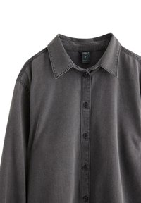 Grå skjorta med knappar i mjukt, texturerat tyg. Har krage, knappad front och långa ärmar. Etikett synlig inuti kragen.