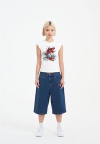 White fitted t-shirt with red fish graphic and blue waves, paired with loose-fitting blue denim culottes and white sneakers.