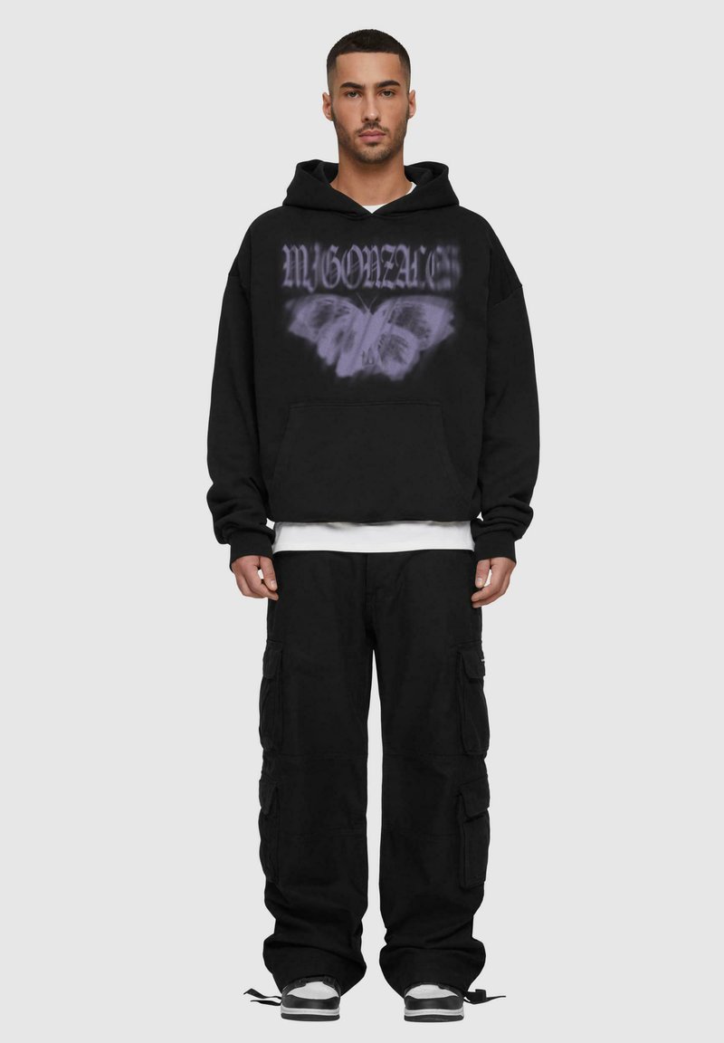 Felpa nera con una grafica di una farfalla viola e scritte sulla parte anteriore, abbinata a pantaloni cargo neri larghi e sneakers nere.