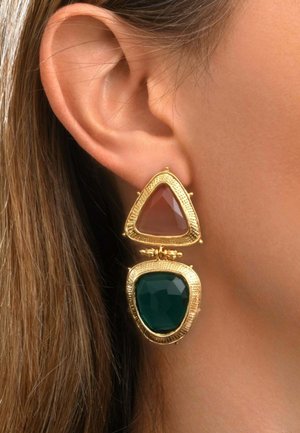 Boucle d'oreille pendante dorée avec une pierre triangulaire brun clair facettée au-dessus d'une pierre plus grande verte foncée de forme irrégulière, portée à l'oreille d'une femme.