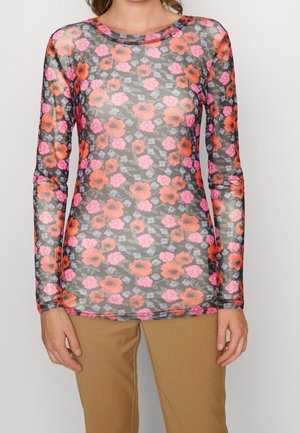 Transparentna bluzka z długim rękawem w jasny pomarańczowy, różowy i fioletowy wzór kwiatowy, noszona z beżowymi spodniami.