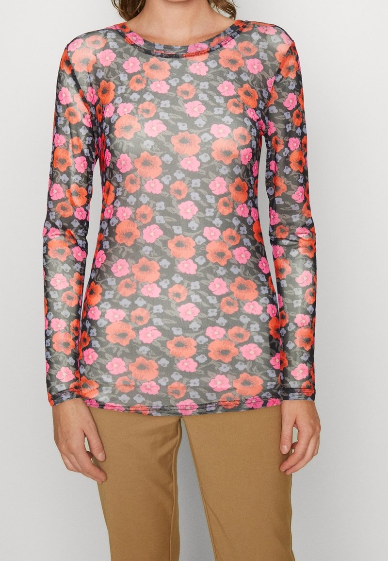 Haut transparent à manches longues avec un motif floral aux couleurs vives orange, rose et violet, porté avec un pantalon beige.
