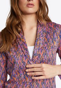 Multikleurige blazer met een geometrisch patroon in paars, oranje en roze, met een sjiekraag en een zachte textuur.