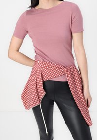 Rosa kortärmad skjorta ihop med ett röd- och vitrutigt midjeband. Svarta läderbyxor fulländar outfiten.