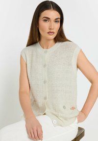 Cardigan senza maniche di colore chiaro, in maglia, con un design testurizzato, caratterizzato da cinque bottoni sul davanti e due tasche laterali.