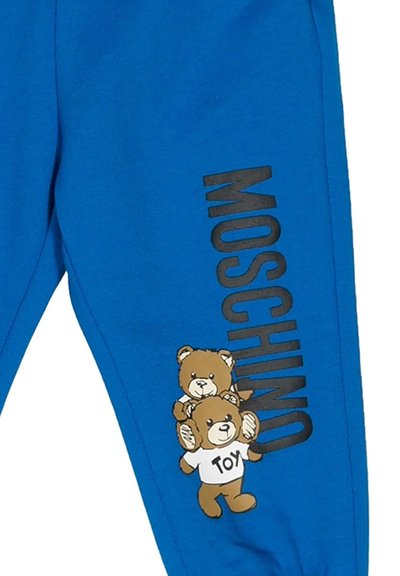 Pantaloni blu con testo verticale nero "MOSCHINO" e due orsi di peluche marroni in stile cartoon, uno dei quali indossa una maglietta bianca con la scritta "TOY".