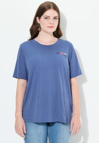 Niebieska koszulka z krótkim rękawem, okrągłym dekoltem i nadrukowanym logo "OPTIMIST" w kolorze czerwonym i czarnym. Gładka tekstura materiału, luźny krój.