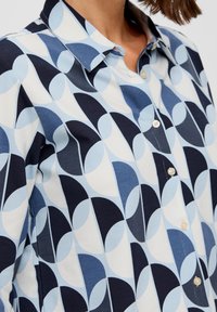 Hemd mit Knöpfen, das ein geometrisches Muster in Marineblau, Hellblau und Weiß aufweist. Hergestellt aus weichem Stoff mit klassischem Kragen und Perlmuttknöpfen.