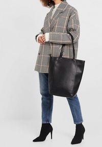 Czarna skórzana torba typu tote z okrągłymi uchwytami, gładką fakturą i prostym wzorem. Noszona z płaszczem w kratę i botkami na wysokim obcasie.
