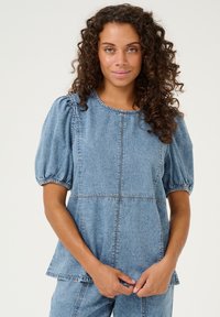 Top din denim cu mâneci bufante, guler rotund și detalii de cusătură vizibile. Culoare albastru deschis, țesătură ușor texturată și croială lejeră.