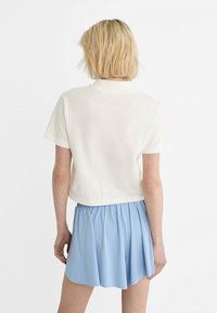 T-shirt bianco corto con maniche corte, abbinato a una gonna svasata blu chiaro. Tessuto morbido con un taglio casual. Design minimalista, senza motivi visibili.
