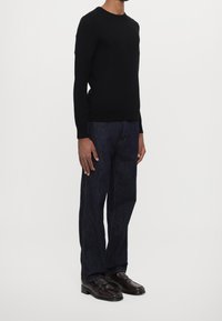 Svart stickad tröja med rund hals, matchad med mörkblå raka jeans och bruna loafers, med en mjuk textur och enkel design.