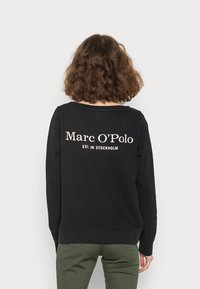 Svart sweatshirt med långa ärmar, rundhalsad och vit text tryckt på baksidan med "Marc O'Polo EST. I STOCKHOLM."